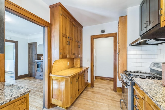 kitchen with stainless steel range with gas cooktop, light wood finished floors, backsplash, and baseboards