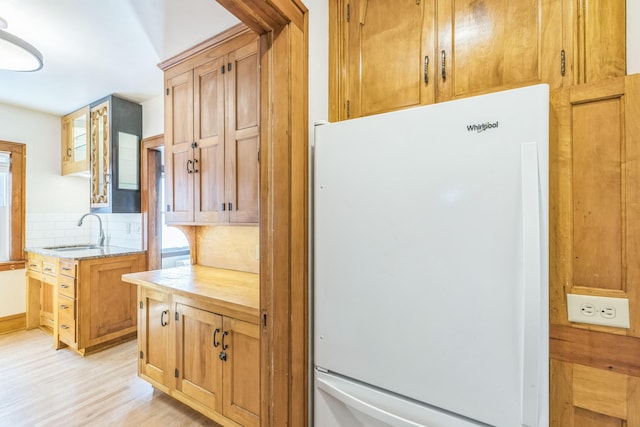 kitchen with freestanding refrigerator, a sink, backsplash, and light wood-type flooring