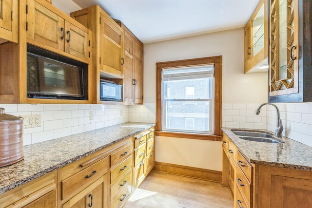 kitchen featuring a sink, light wood-style floors, built in microwave, baseboards, and light stone counters