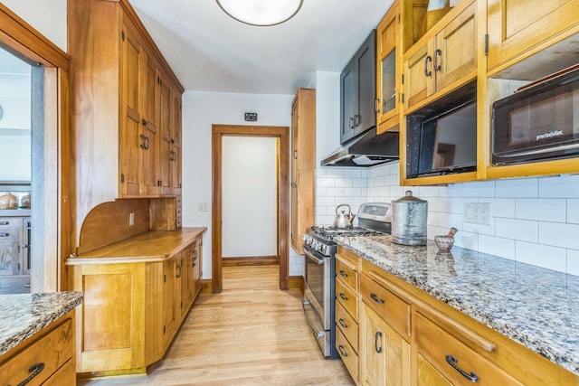 kitchen with stainless steel gas range oven, under cabinet range hood, light wood-style flooring, and decorative backsplash