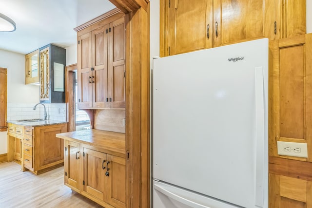 kitchen with freestanding refrigerator, backsplash, light wood-type flooring, and a sink