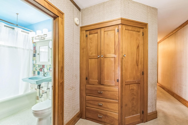 corridor with wallpapered walls, light carpet, baseboards, and a sink