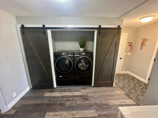 12787 Lumberjack Rd NW, Shevlin, MN 56676 - washroom featuring a barn door, washer and clothes dryer, wood finished floors, a textured ceiling, and baseboards