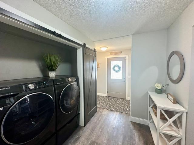 12787 Lumberjack Rd NW, Shevlin, MN 56676 - washroom featuring a barn door, a textured ceiling, washer and clothes dryer, dark wood-style flooring, and baseboards