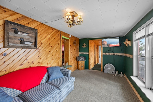 living area featuring an inviting chandelier, wooden walls, and carpet