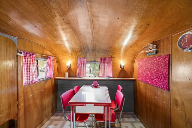 dining space with tile patterned floors, vaulted ceiling, and wooden walls