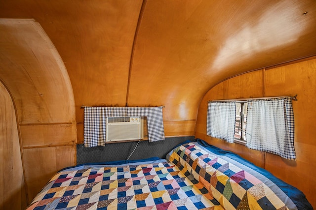unfurnished bedroom with arched walkways, lofted ceiling, wood walls, and a wall unit AC