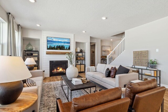 living area with wood finished floors, stairway, recessed lighting, a textured ceiling, and a large fireplace