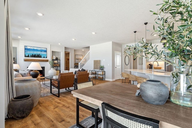 dining area with a fireplace, light wood-style floors, recessed lighting, baseboards, and stairway