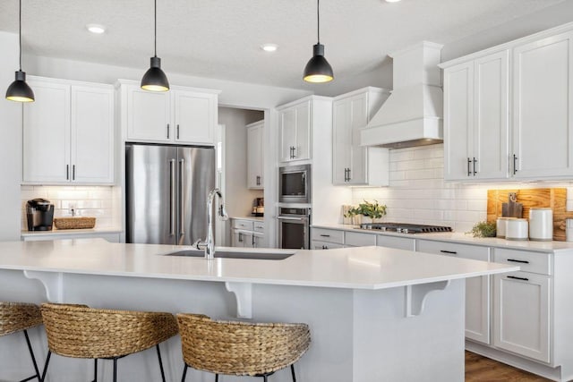 kitchen featuring appliances with stainless steel finishes, a sink, a breakfast bar area, premium range hood, and backsplash