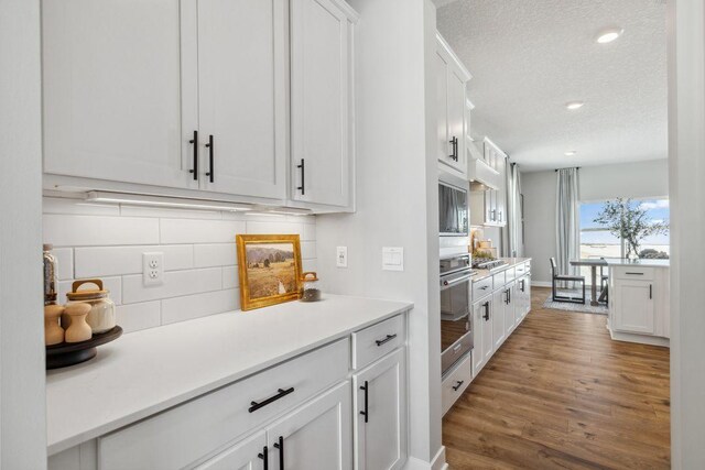 kitchen with white cabinets, appliances with stainless steel finishes, a textured ceiling, wood finished floors, and backsplash