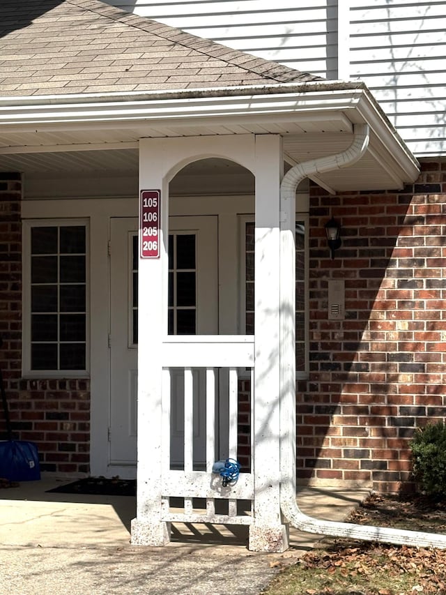 doorway to property with brick siding and roof with shingles