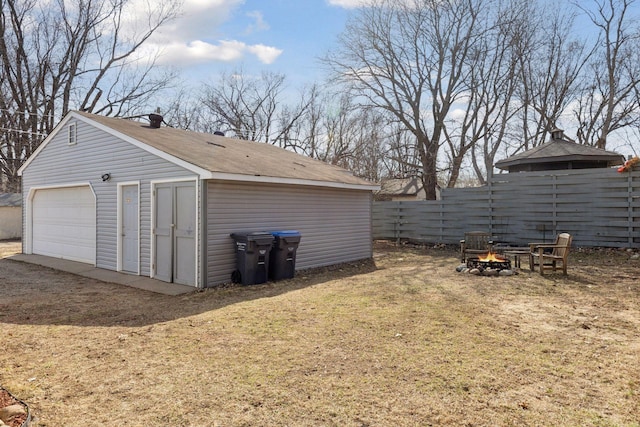 view of yard with an outdoor structure, a detached garage, fence, and a fire pit