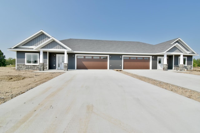 craftsman inspired home featuring a shingled roof, an attached garage, stone siding, board and batten siding, and driveway