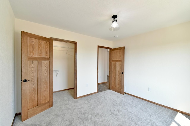 unfurnished bedroom with a spacious closet, a closet, baseboards, and carpet flooring