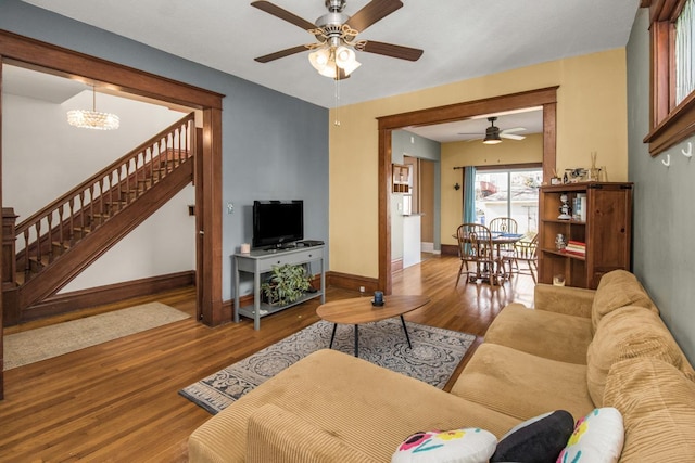 living area with baseboards, stairs, ceiling fan with notable chandelier, and wood finished floors