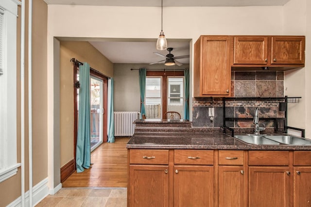 kitchen featuring backsplash, a ceiling fan, brown cabinets, a sink, and radiator heating unit