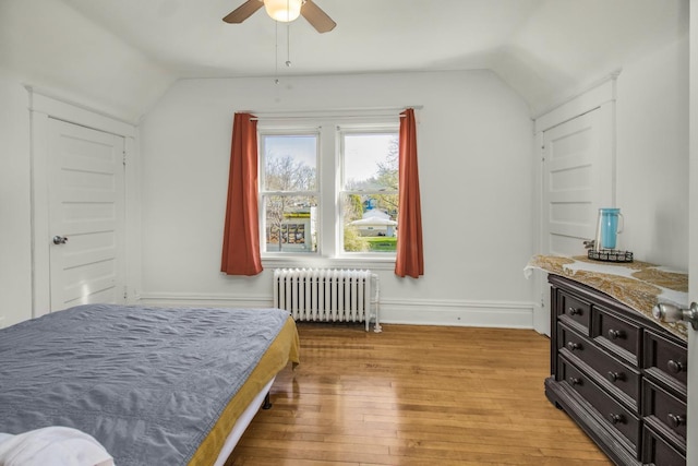 bedroom with light wood-style flooring, radiator heating unit, a ceiling fan, baseboards, and lofted ceiling