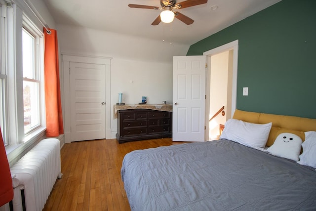 bedroom with wood-type flooring, lofted ceiling, radiator heating unit, and multiple windows