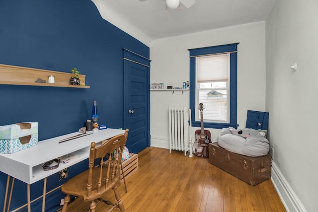 interior space with wood-type flooring, ceiling fan, baseboards, and radiator heating unit