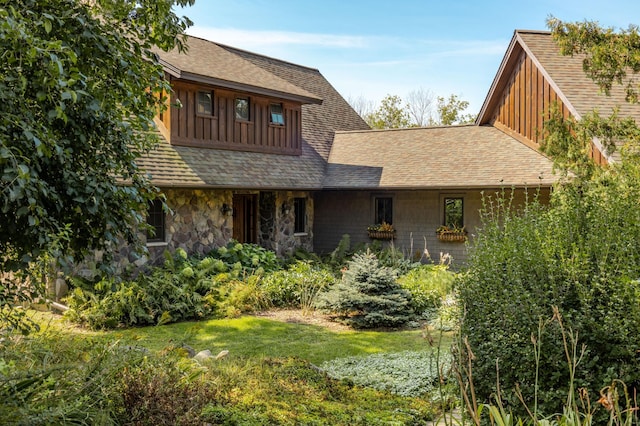 view of front facade featuring stone siding, a shingled roof, and a front yard