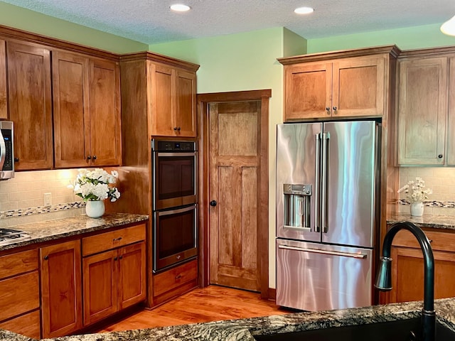 8871 Kahl Way NE, Otsego, MN 55362 - kitchen featuring stainless steel appliances, light wood finished floors, dark stone counters, decorative backsplash, and brown cabinetry
