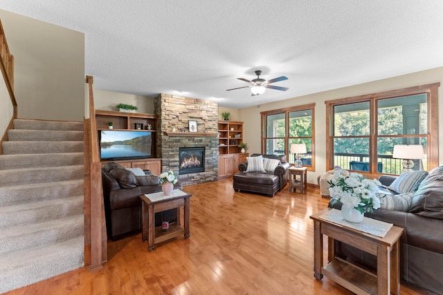 8871 Kahl Way NE, Otsego, MN 55362 - living area with ceiling fan, light wood finished floors, a stone fireplace, a textured ceiling, and stairs