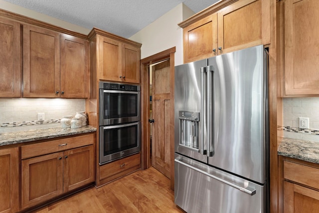 8871 Kahl Way NE, Otsego, MN 55362 - kitchen featuring appliances with stainless steel finishes, brown cabinets, tasteful backsplash, light wood-type flooring, and light stone counters