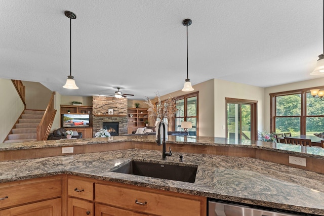 8871 Kahl Way NE, Otsego, MN 55362 - kitchen with a textured ceiling, a ceiling fan, a stone fireplace, dark stone counters, and decorative light fixtures