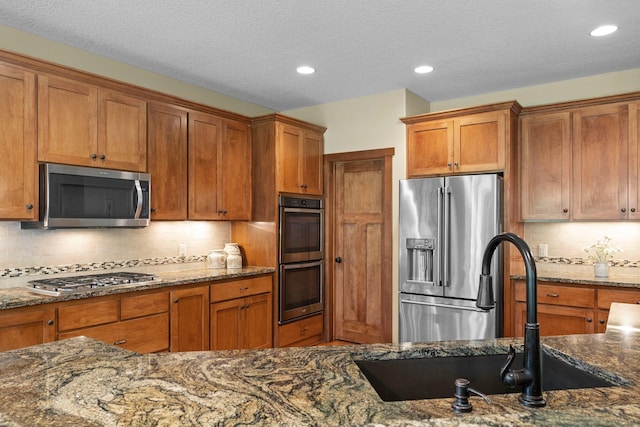 8871 Kahl Way NE, Otsego, MN 55362 - kitchen featuring appliances with stainless steel finishes, brown cabinetry, dark stone countertops, decorative backsplash, and recessed lighting