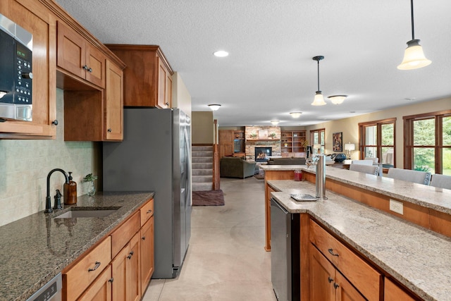 8871 Kahl Way NE, Otsego, MN 55362 - kitchen featuring appliances with stainless steel finishes, open floor plan, a fireplace, brown cabinets, and decorative light fixtures