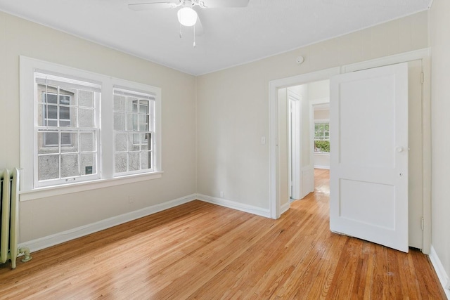 spare room with light wood-style flooring, radiator, ceiling fan, and baseboards