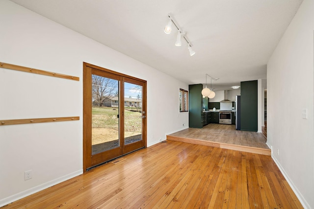 unfurnished living room with baseboards, rail lighting, light wood-style flooring, and visible vents