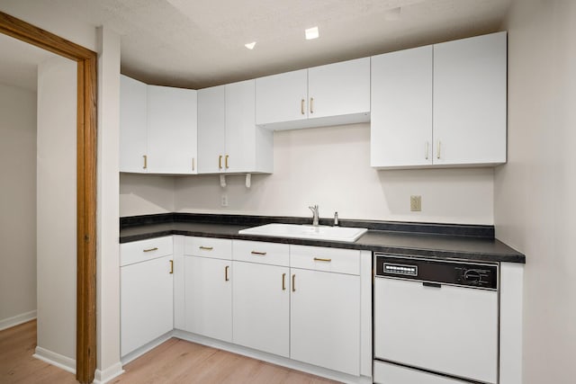 kitchen with white dishwasher, dark countertops, light wood-type flooring, a sink, and white cabinetry