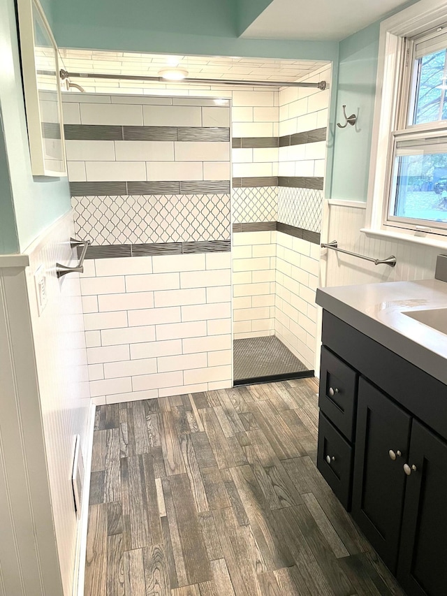 full bath with a wainscoted wall, vanity, wood finished floors, and a walk in shower