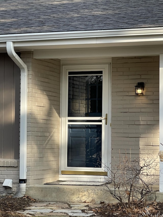 entrance to property featuring brick siding and a shingled roof