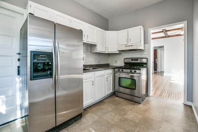 kitchen with dark countertops, white cabinets, under cabinet range hood, decorative backsplash, and appliances with stainless steel finishes