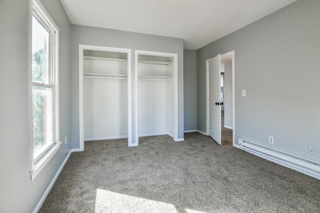 unfurnished bedroom featuring a baseboard radiator, baseboards, carpet floors, and multiple closets