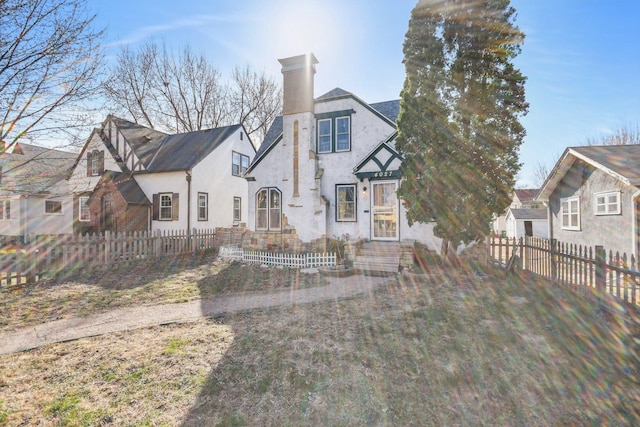 tudor-style house with stucco siding, a chimney, and a fenced front yard