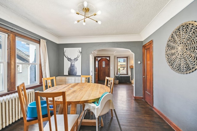 dining space with radiator heating unit, arched walkways, a notable chandelier, and a textured ceiling