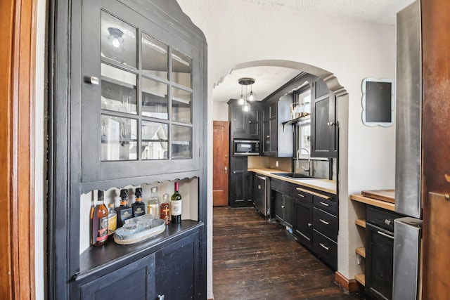 bar featuring arched walkways, stainless steel microwave, a sink, and dark wood-style floors