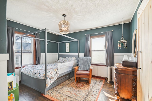bedroom featuring a textured ceiling, wood finished floors, radiator heating unit, and multiple windows
