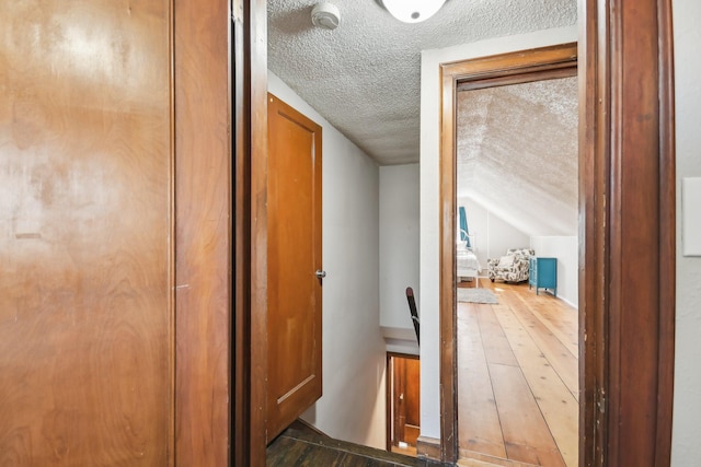 corridor with an upstairs landing, vaulted ceiling, a textured ceiling, and hardwood / wood-style floors