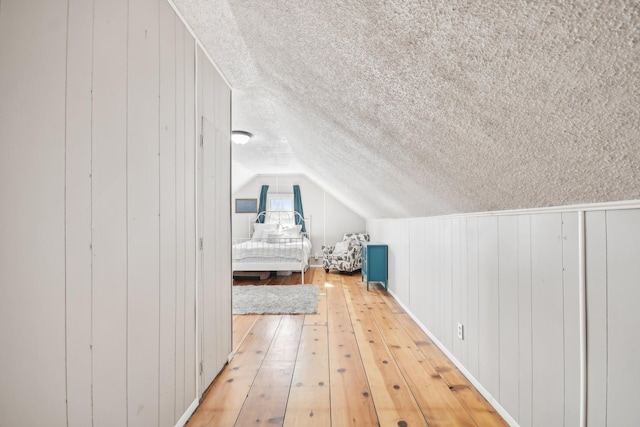 unfurnished bedroom with light wood-type flooring, vaulted ceiling, and a textured ceiling