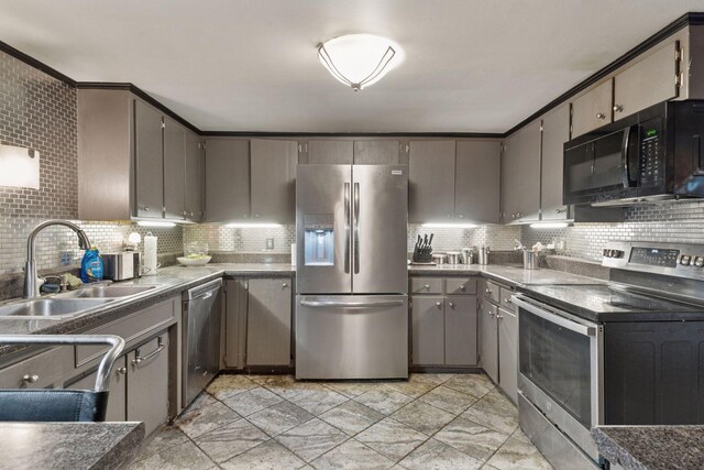 kitchen featuring stainless steel appliances, a sink, tasteful backsplash, gray cabinetry, and dark countertops