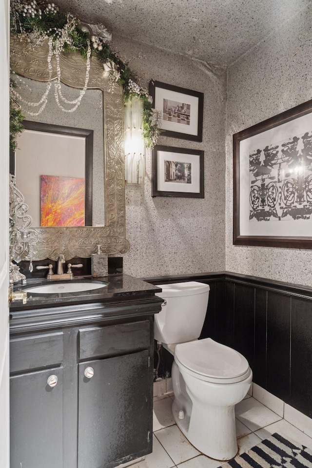 bathroom featuring vanity, toilet, a wainscoted wall, and tile patterned flooring