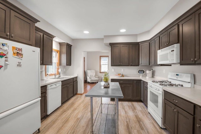kitchen with dark brown cabinets, white appliances, light wood-type flooring, light countertops, and a sink