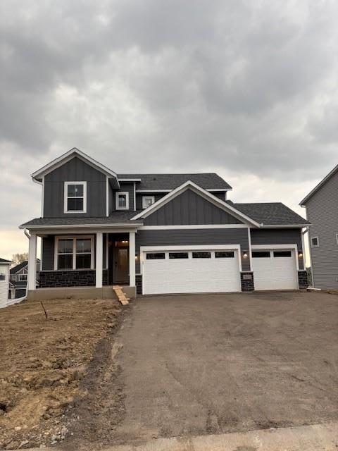 view of front of house featuring a garage, aphalt driveway, stone siding, board and batten siding, and a porch