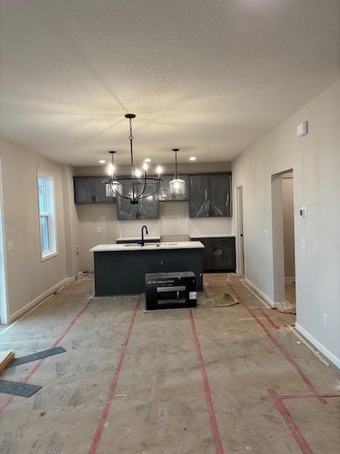 kitchen featuring light countertops, a chandelier, an island with sink, decorative light fixtures, and baseboards
