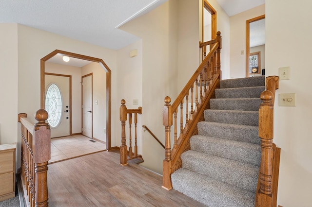 entrance foyer featuring arched walkways, stairs, and wood finished floors